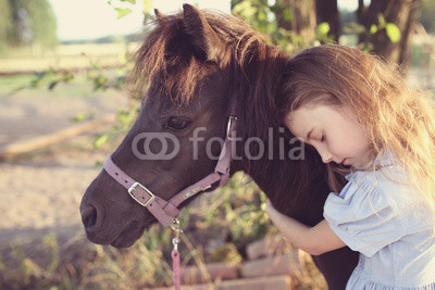 Young girl hugs a pony on a farm