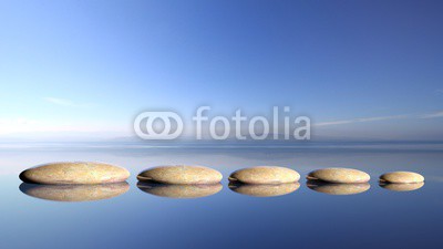 Zen stones row from large to small  in water with blue sky and peaceful landscape background.