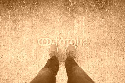 Man with orange shoes standing on a textured, concrete city street.