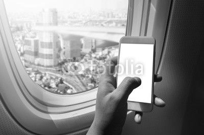 Asian man hand holding blank screen smart-phone on board of airplane near window seat and wing