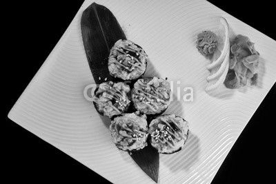 Baked Sushi Roll with crab, eel fish and spicy salmon served with vasabi, pickled ginger and lemon slice on white plate on black background