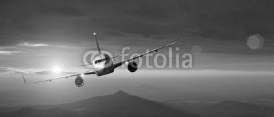 Commercial airplane flying above mountains in sunset