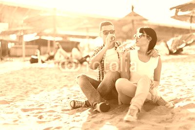 Happy young couple drinking beer and having fun at the beach during sunset