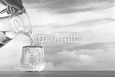 Fresh and clean drinking water being poured from jug into glass on sky background