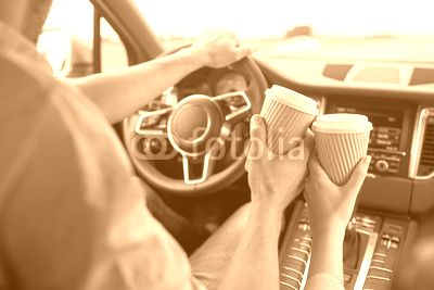 close up of couple driving in car with coffee cups