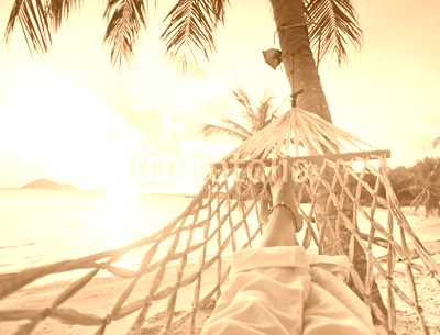 Female legs in a hammock on a background of the sea, palm trees and sunset. Vacation concept