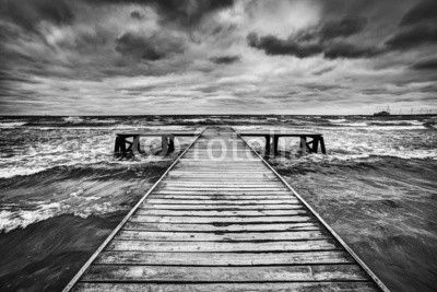 Old wooden jetty during storm on the sea. Dramatic sky