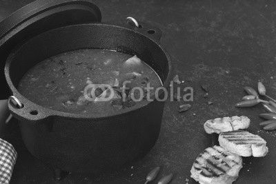 Fish and tomato stew in cast iron pot with grilled bread slices on rustic table
