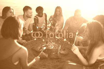 Group of restful friends roasting marshmallows while sitting by bonfire