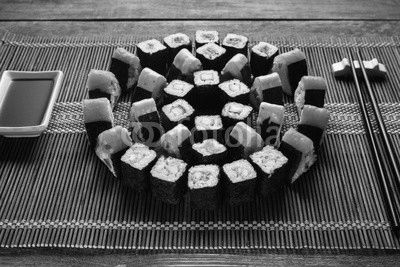 Bright colorful japanese sushi set, round ornament of maki rolls served on brown straw mat, closeup. Japanese food art, national cuisine, restaurant menu photo.