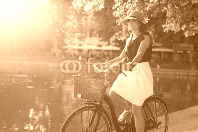 Attractive young woman riding bicycle along a pond in city park