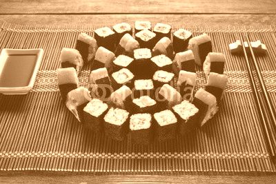 Bright colorful japanese sushi set, round ornament of maki rolls served on brown straw mat, closeup. Japanese food art, national cuisine, restaurant menu photo.