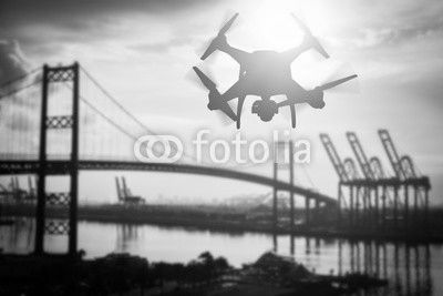 Silhouette of Unmanned Aircraft System (UAV) Quadcopter Drone In The Air Over Shipping Port.